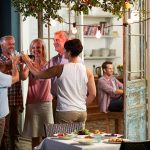 A group of people laugh and have a toast while dining outdoors.